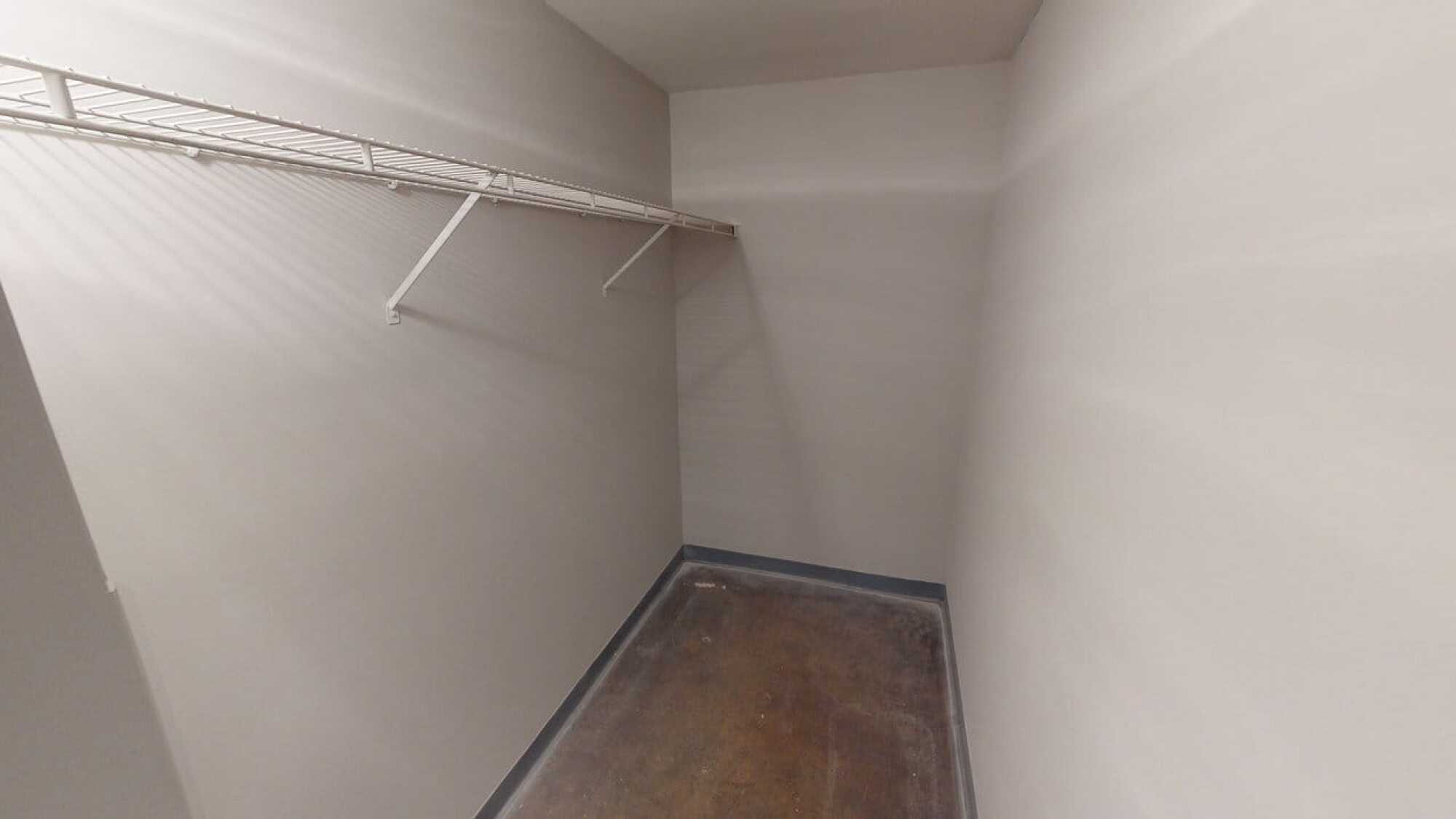 Empty walk-in closet with white walls, a wire shelf, and a bare floor. No items or decorations are present.