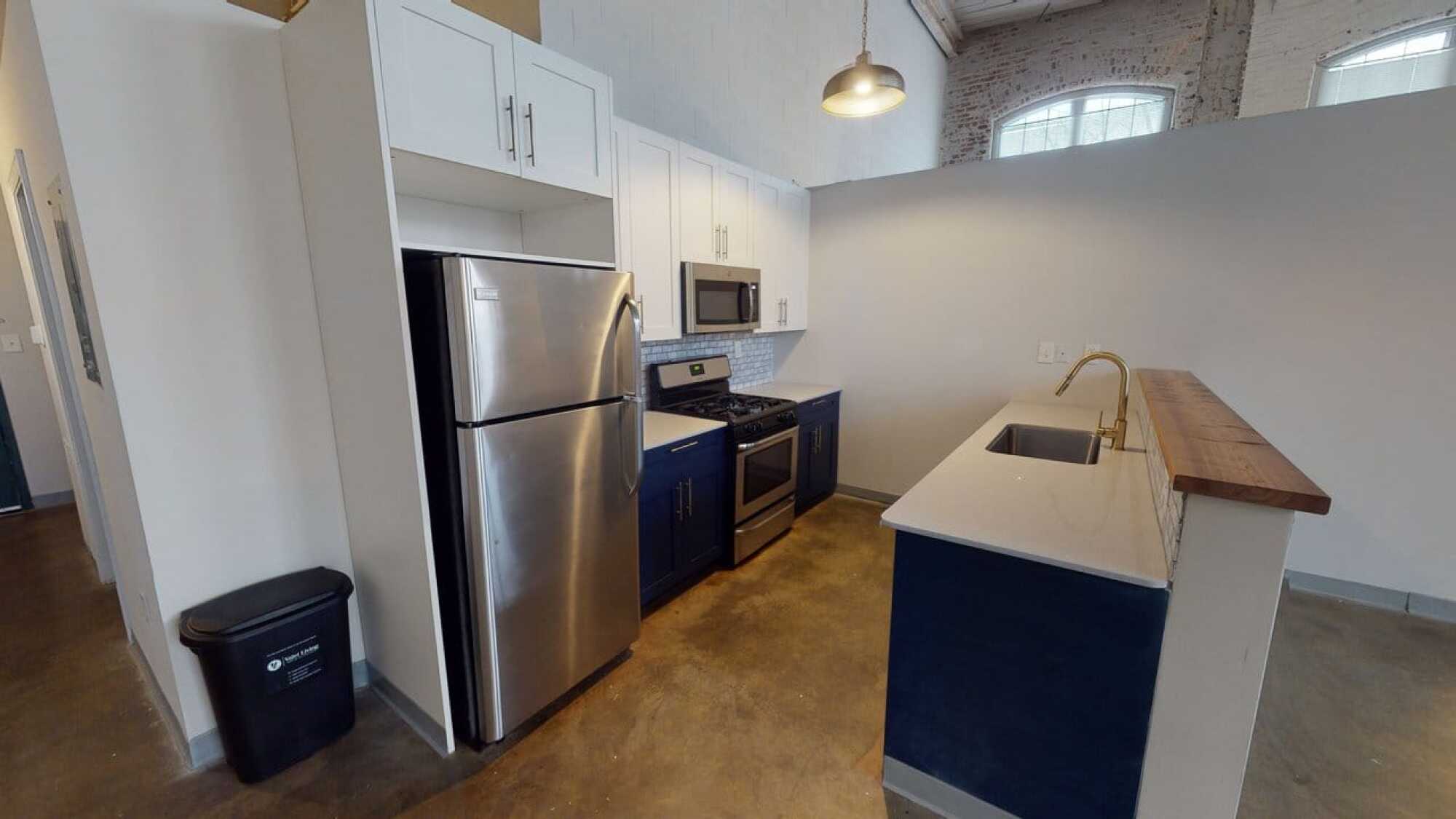 Modern kitchen with stainless steel appliances, blue lower cabinets, white uppers, and a gold faucet on a white island.