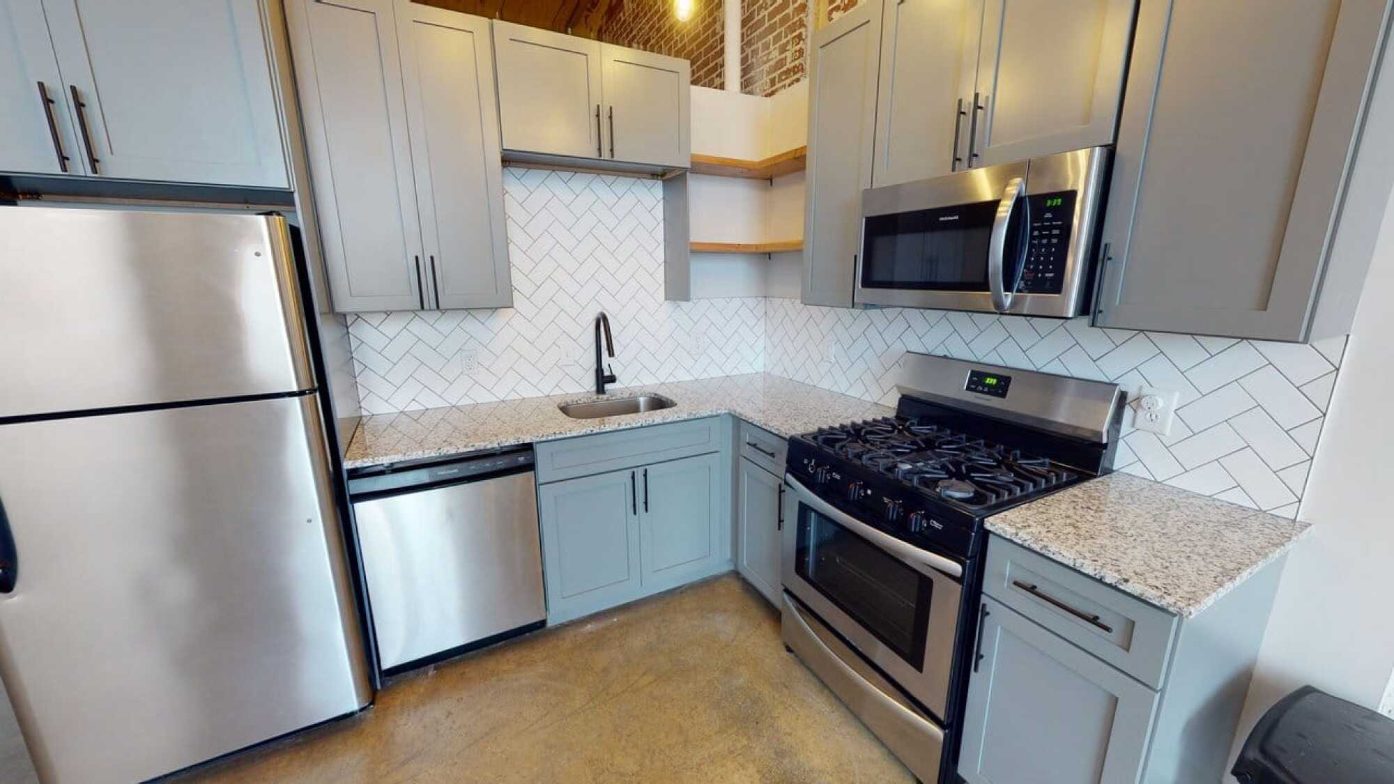 Modern kitchen with gray cabinets, stainless steel appliances, granite counters, and white herringbone tile backsplash.