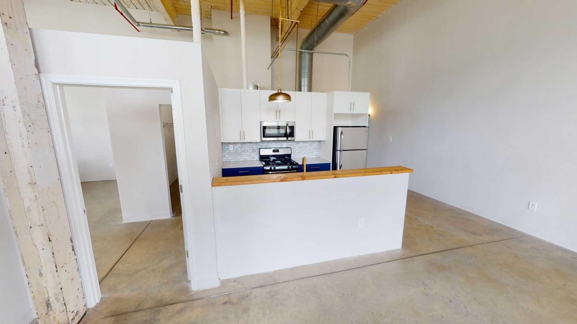 Modern kitchen with white cabinets, stainless steel appliances, wooden countertop, and open space with concrete floors.
