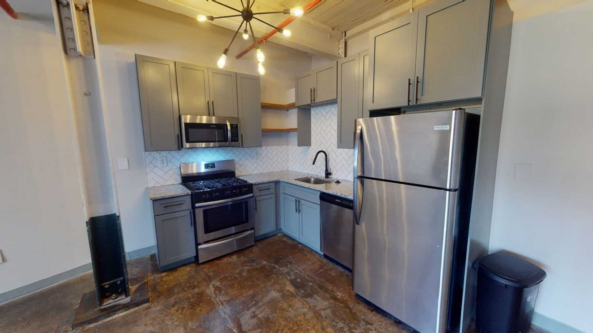 Modern kitchen with gray cabinets, stainless steel appliances, granite countertops, and herringbone tile backsplash.