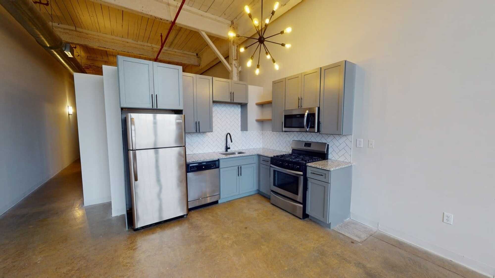 Modern kitchen with gray cabinets, stainless steel appliances, tile backsplash, and exposed ceiling beams.