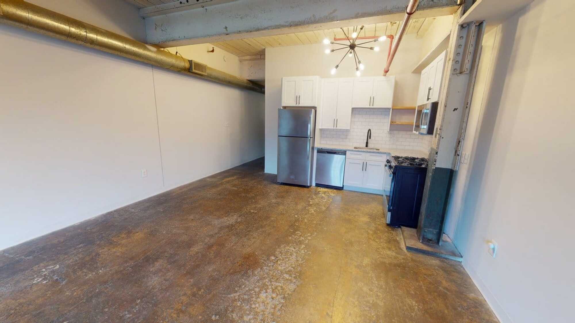 Modern loft-style kitchen with stainless steel appliances, white cabinets, and exposed pipes on ceiling.