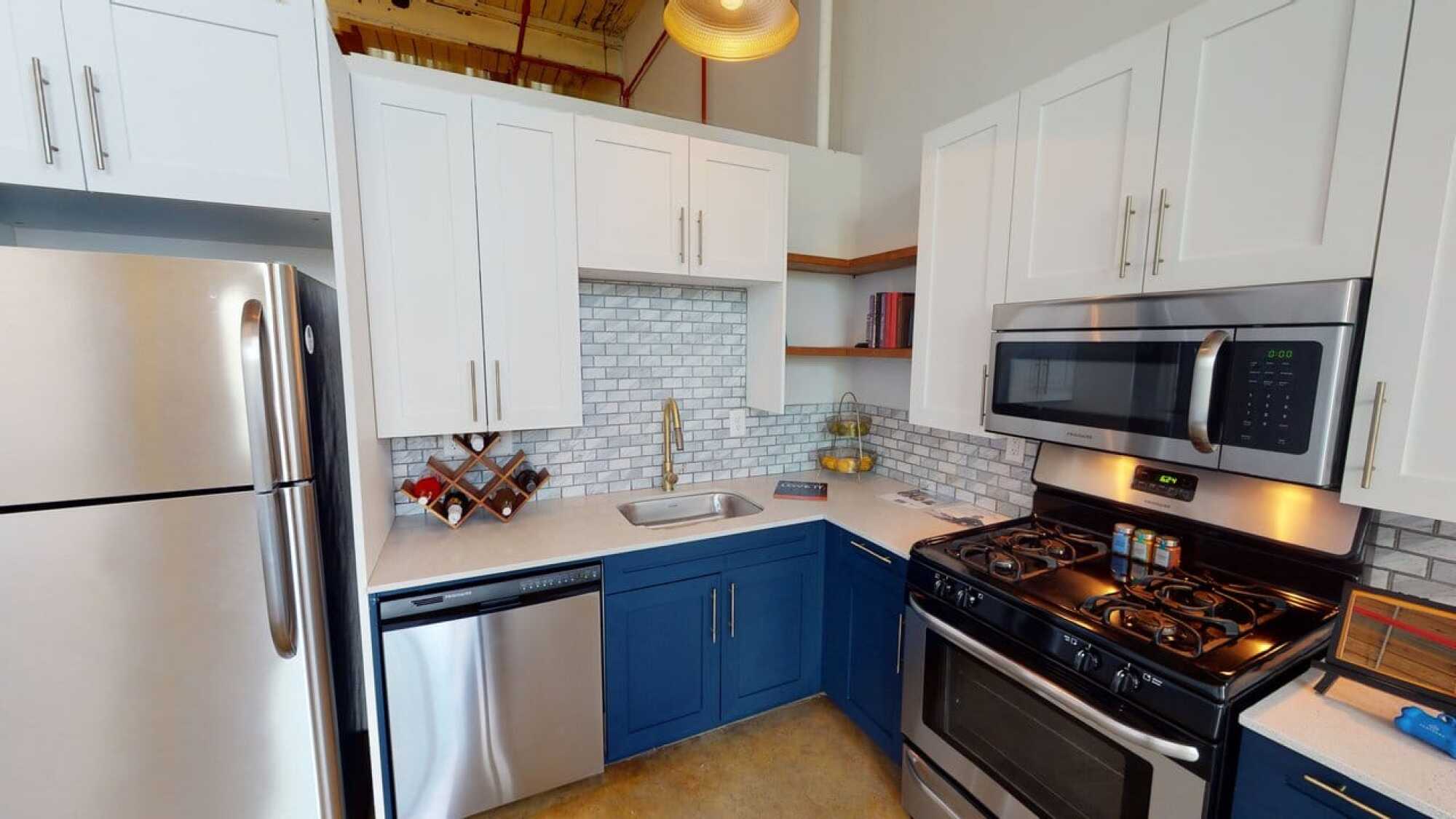 Modern kitchen with white upper cabinets, blue lower cabinets, stainless appliances, and a white subway tile backsplash.