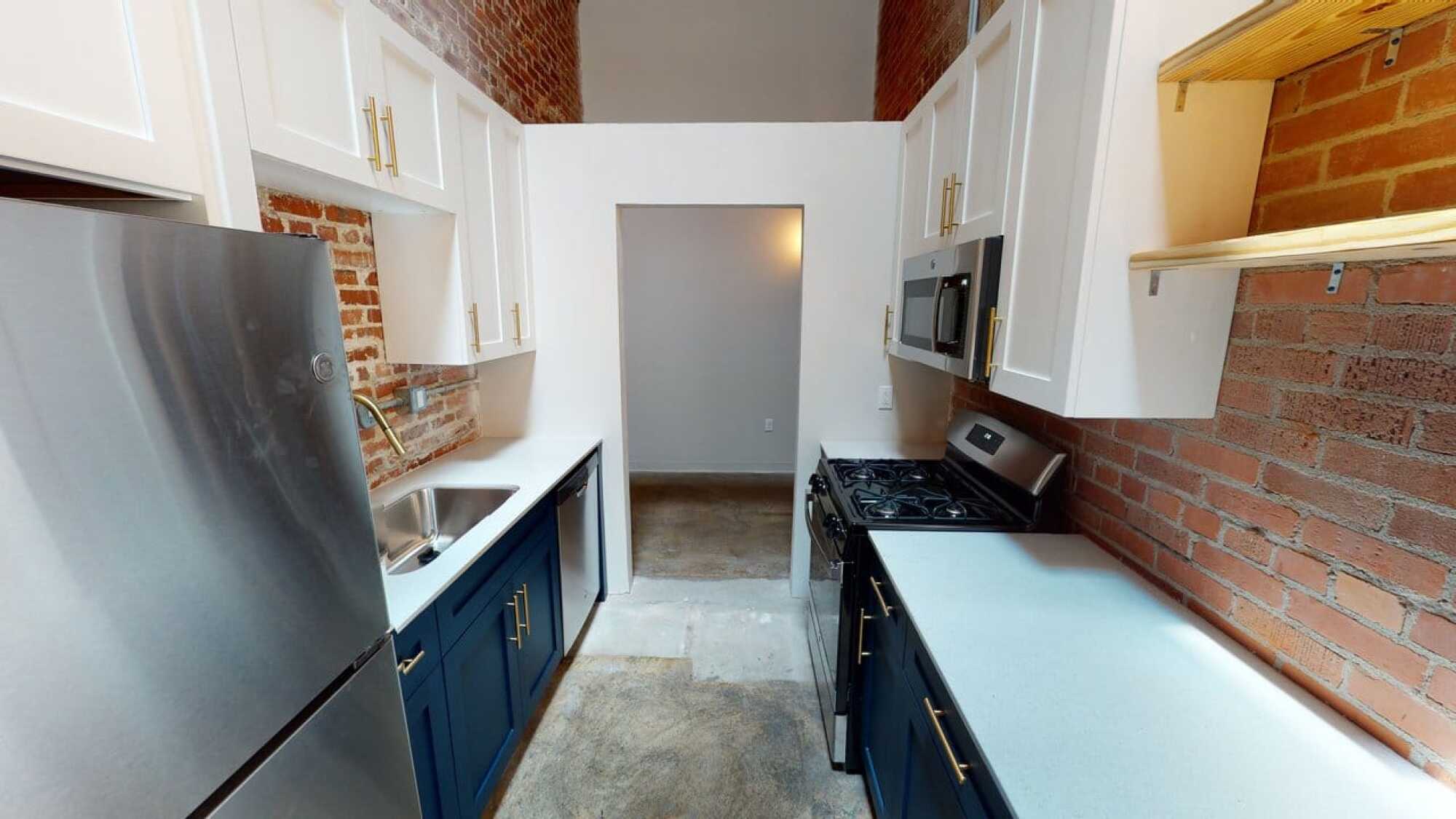 Narrow kitchen with brick walls, stainless steel appliances, white cabinets, and light countertops.