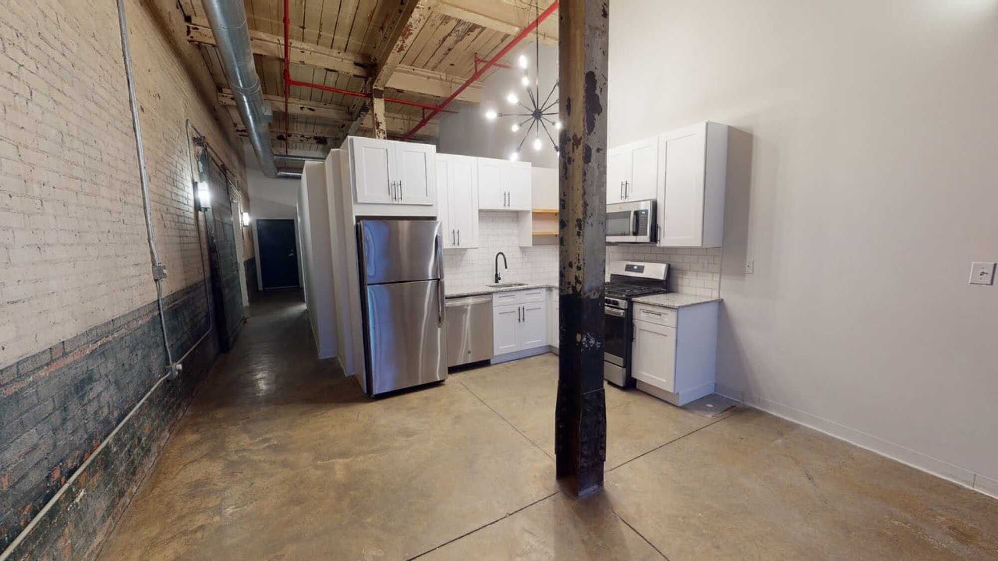 Modern industrial kitchen with white cabinets, stainless steel appliances, exposed brick, and a support beam in the center.