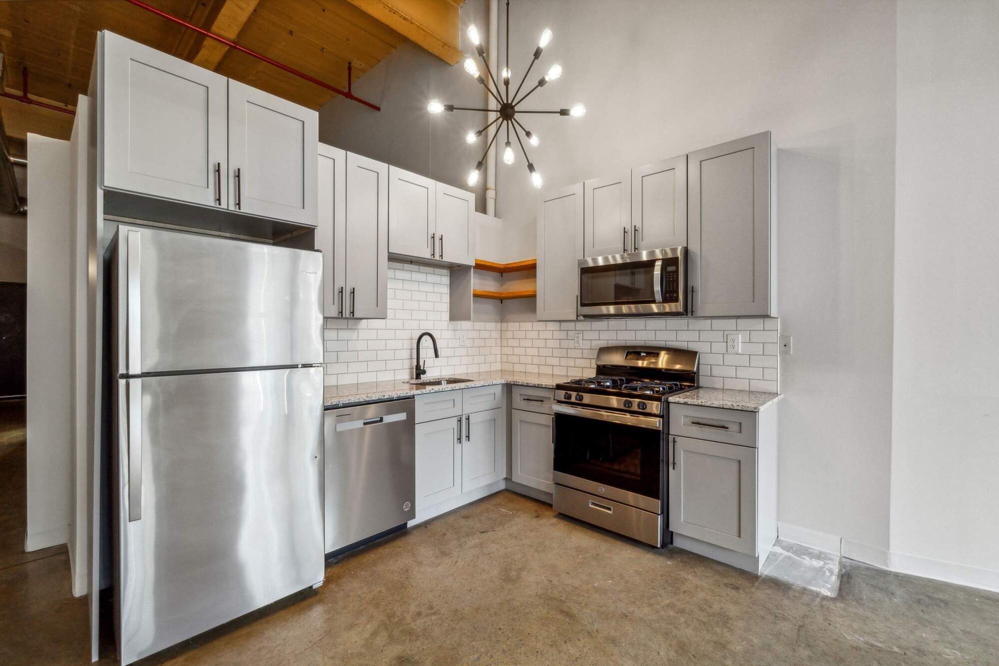 Modern kitchen with gray cabinets, stainless steel appliances, white subway tile, and a sputnik chandelier.